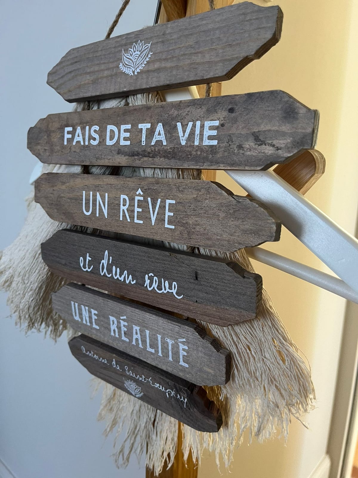 Panneau en bois suspendu au cabinet, portant la citation d'Antoine de Saint-Exupéry « Fais de ta vie un rêve et d'un rêve une réalité »